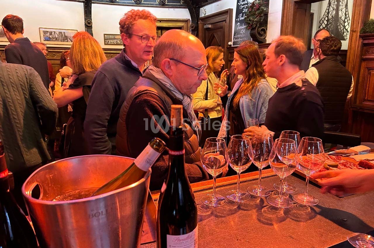 Des personnes discutent et dégustent du vin dans un bar ou une salle conviviale, avec des bouteilles et des verres sur le…
