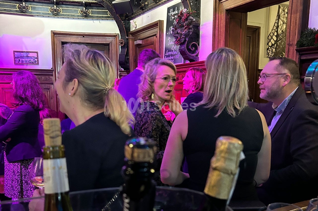 Des personnes discutent dans un bar ou un espace événementiel, avec des bouteilles au premier plan et un éclairage coloré.