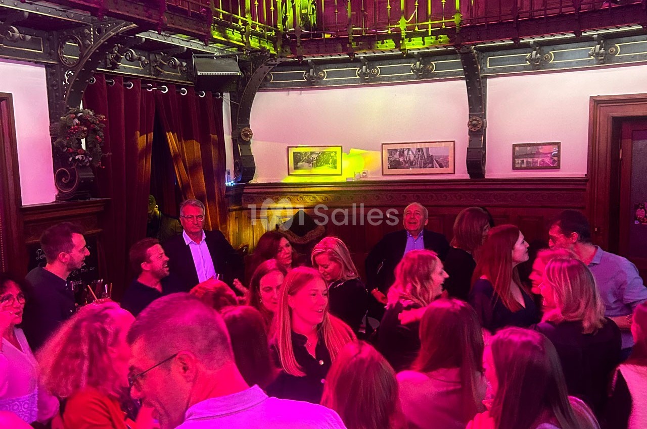 Groupe de personnes discutant et partageant un moment convivial dans une salle à la décoration chaleureuse et boisée.