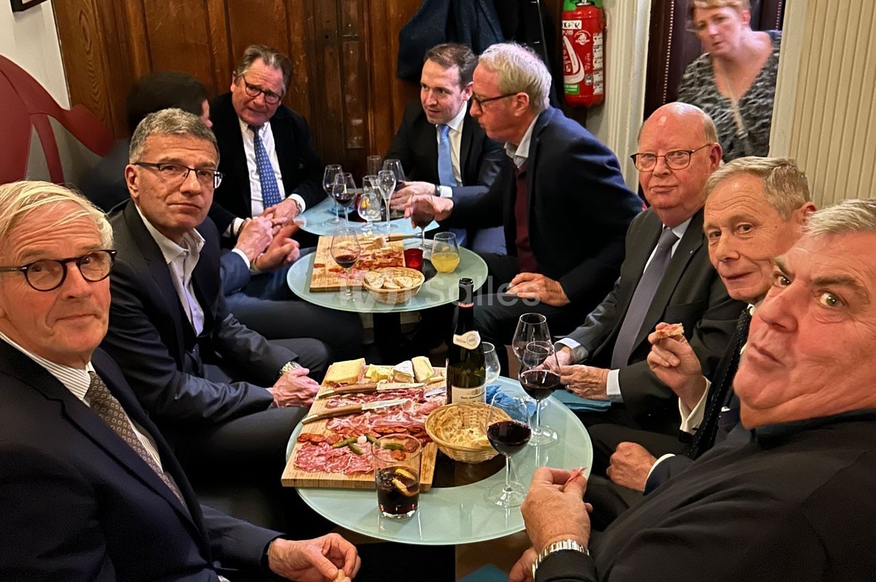 Des hommes en costume assis autour de tables avec des plateaux de charcuterie, fromage et verres de vin.