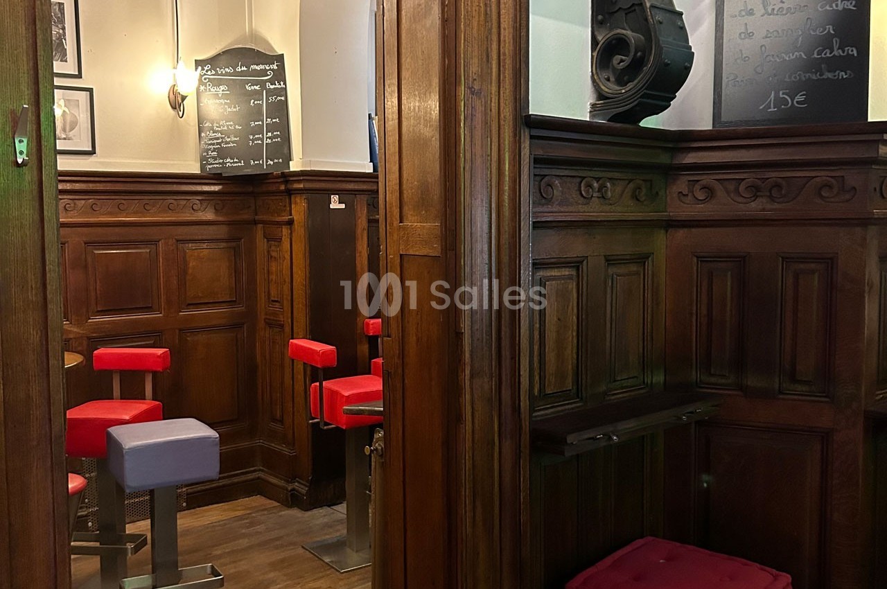 Intérieur d'un café avec des tabourets rouges, boiseries sombres et ardoises affichant des menus écrits à la craie.