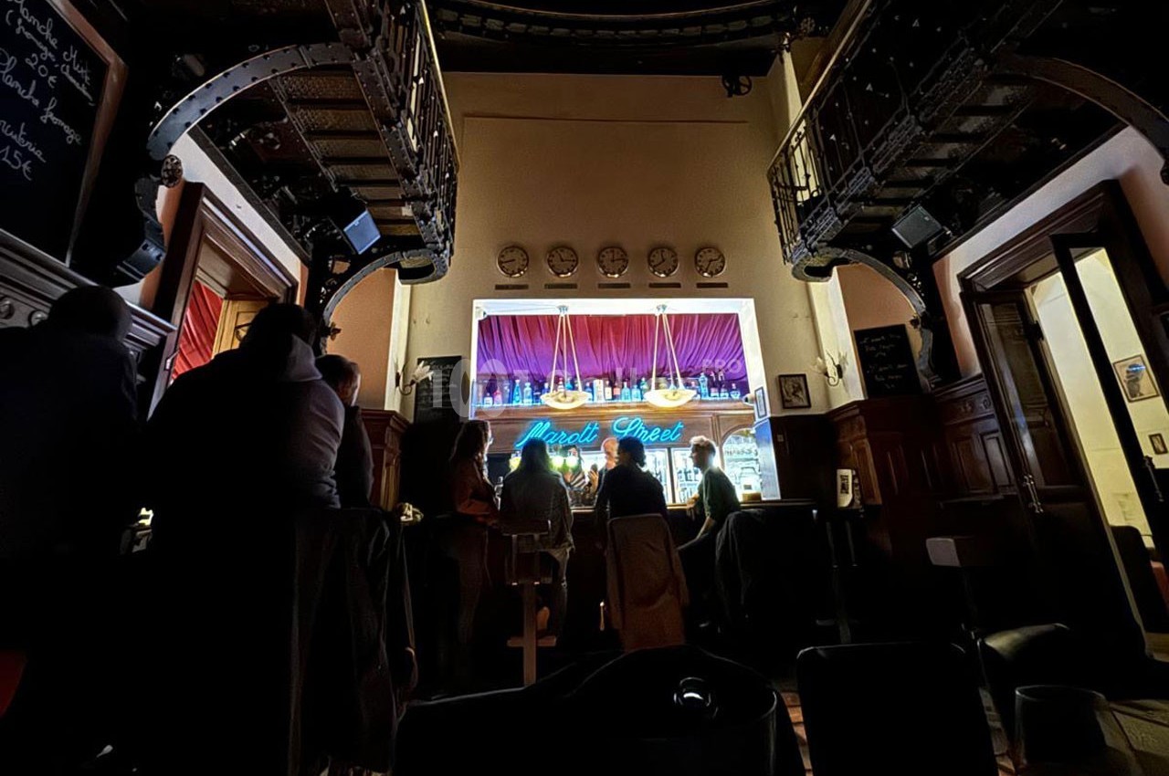Des personnes assises dans un bar sombre avec un comptoir éclairé et un néon bleu en arrière-plan.