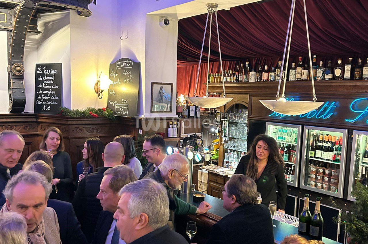 Un bar animé avec des clients discutant et une serveuse derrière le comptoir, entourés de décorations chaleureuses.