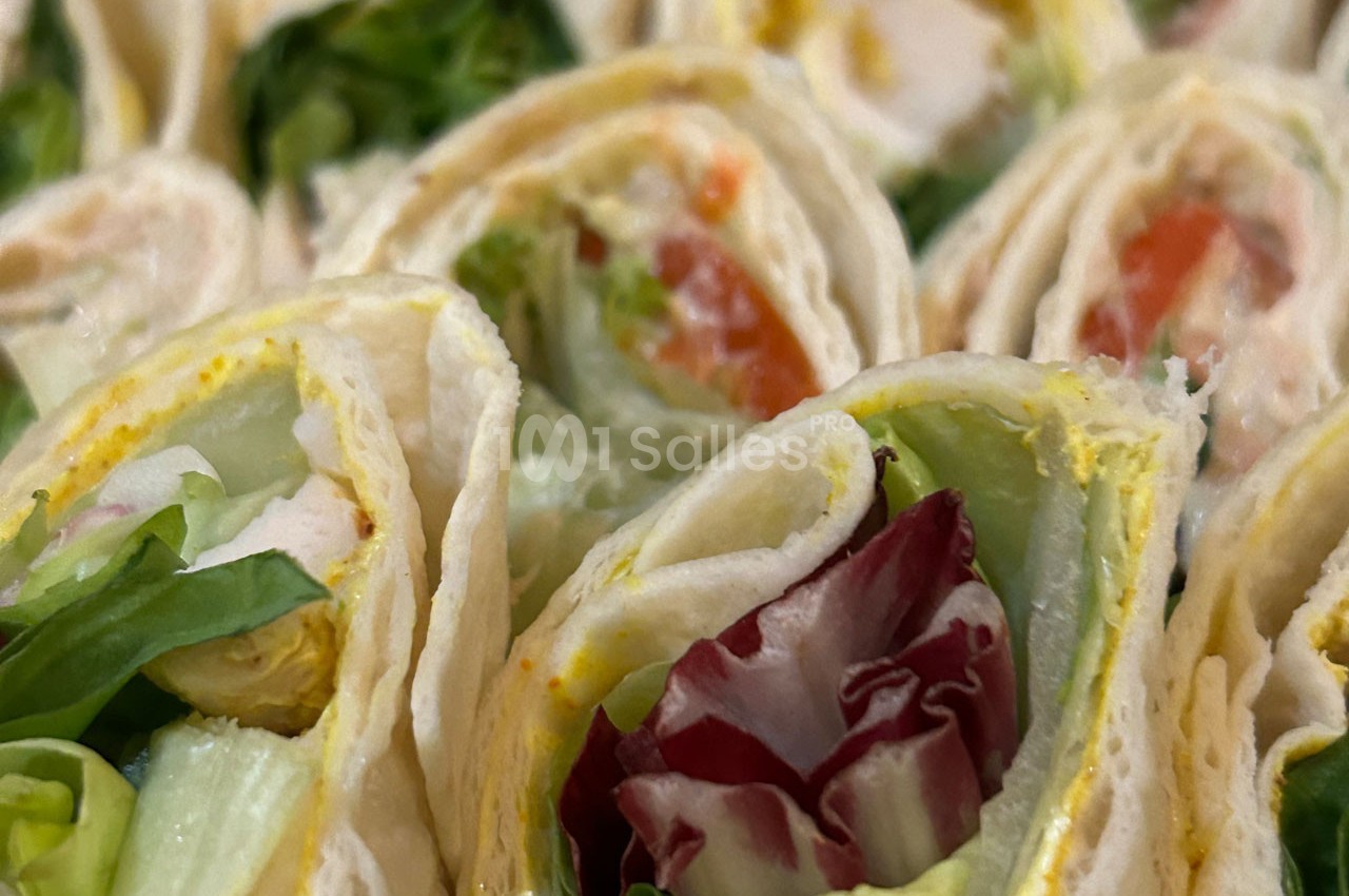 Wraps roulés garnis de salade, tomates, et autres légumes frais, présentés en gros plan.