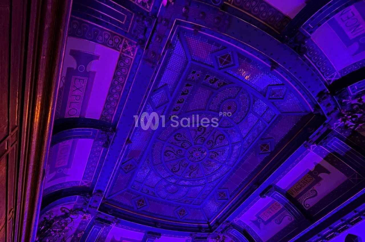 Plafond décoratif illuminé par des lumières violettes, avec motifs géométriques et détails architecturaux ornés.