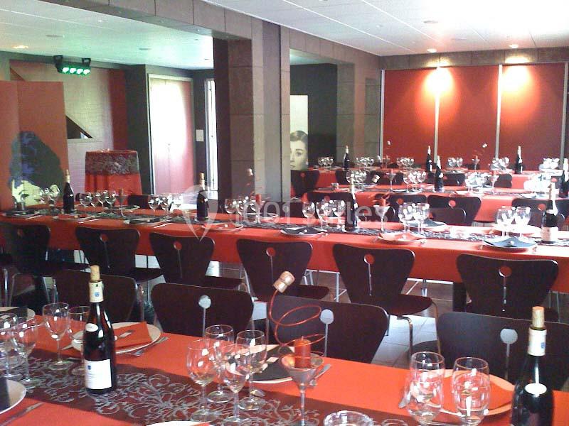 Salle de réception décorée avec des tables dressées, nappes rouges, verres et bouteilles de vin.