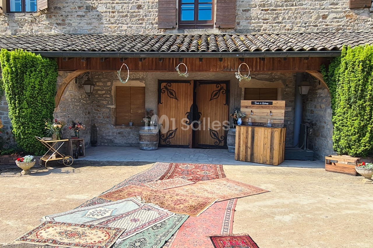 Entrée d'une maison en pierre avec porte en bois sculpté, tapis colorés au sol et décorations rustiques.