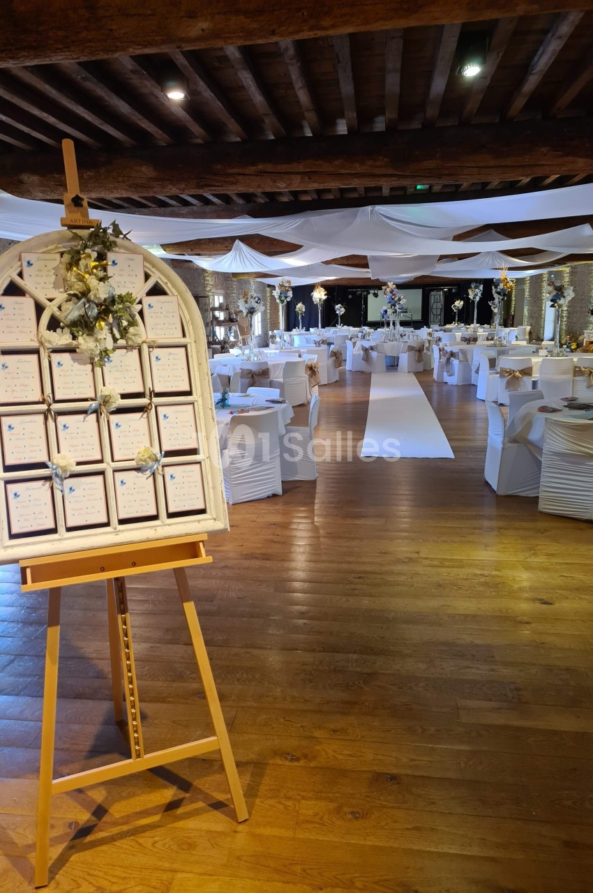 Salle de réception décorée pour un mariage avec un plan de table sur chevalet au premier plan.