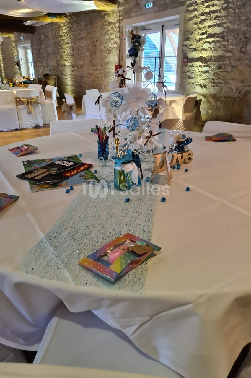 Table décorée pour un événement, avec nappe blanche, centre de table bleu et blanc, crayons et livrets colorés.