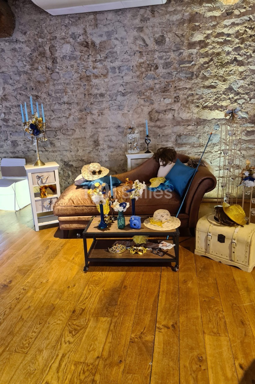 Salon décoré avec des objets vintage, des fleurs jaunes et bleues, sur un parquet en bois et un mur en pierre apparente.