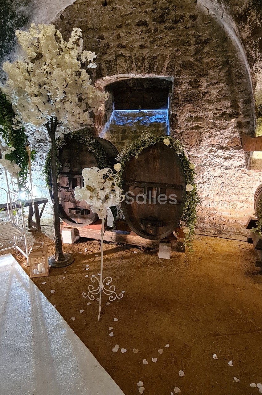 Deux tonneaux en bois décorés de fleurs blanches et de verdure dans une cave voûtée en pierre.