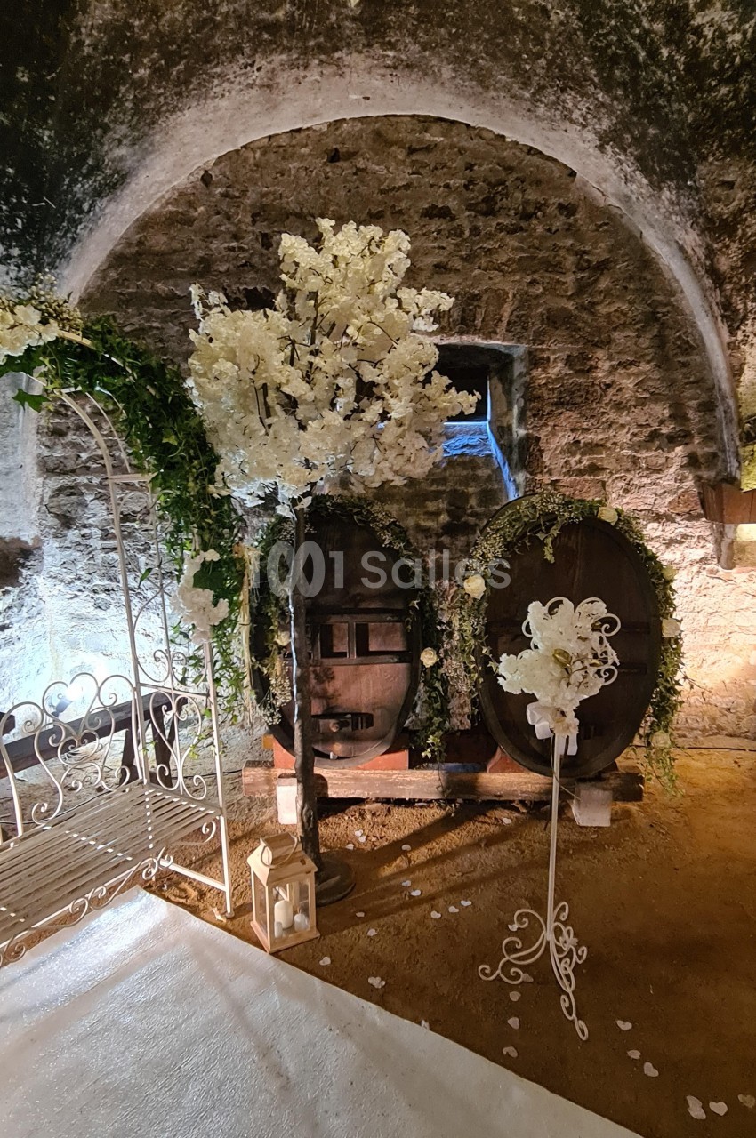 Décoration florale blanche avec tonneaux en bois et arche dans une cave voûtée en pierre.