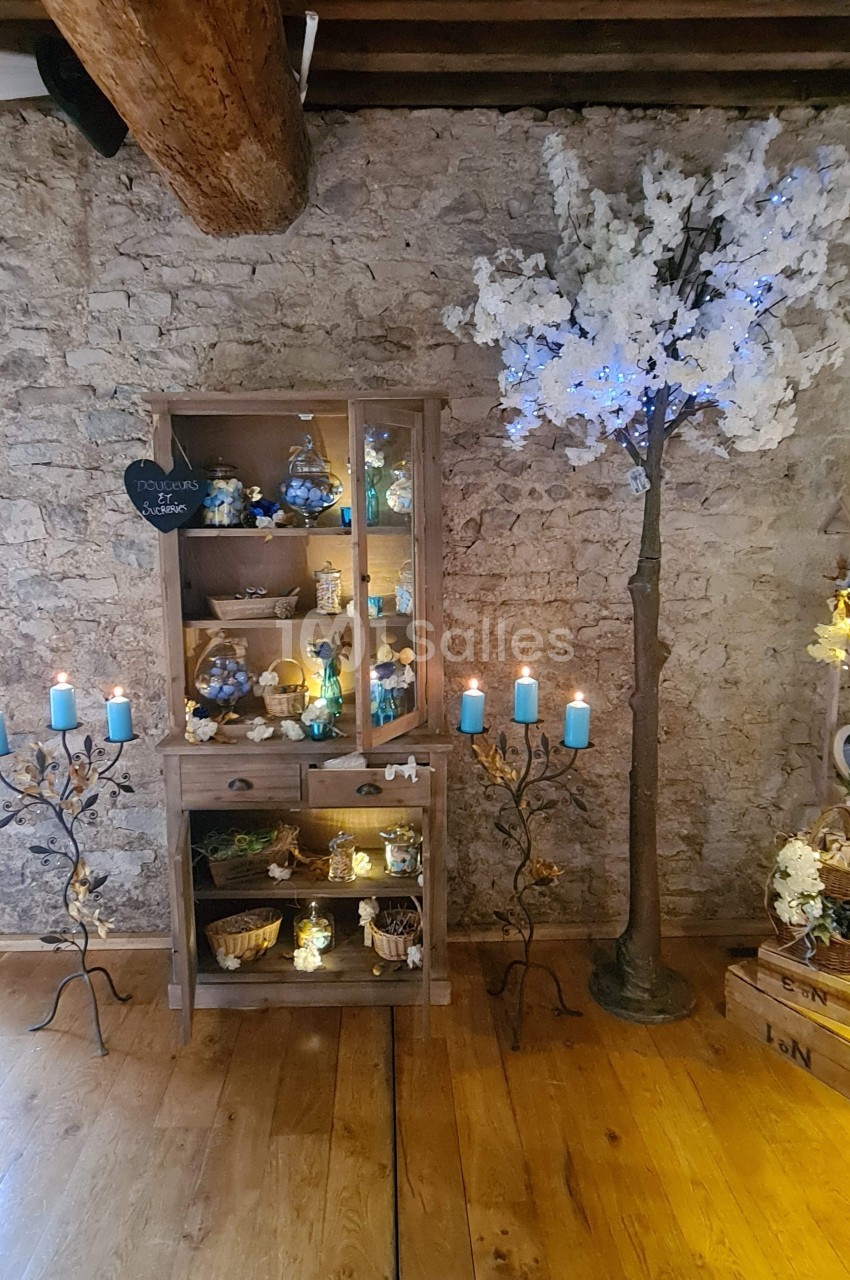 Meuble en bois décoré de bougies et d'objets, avec un arbre artificiel illuminé dans une pièce aux murs en pierre.