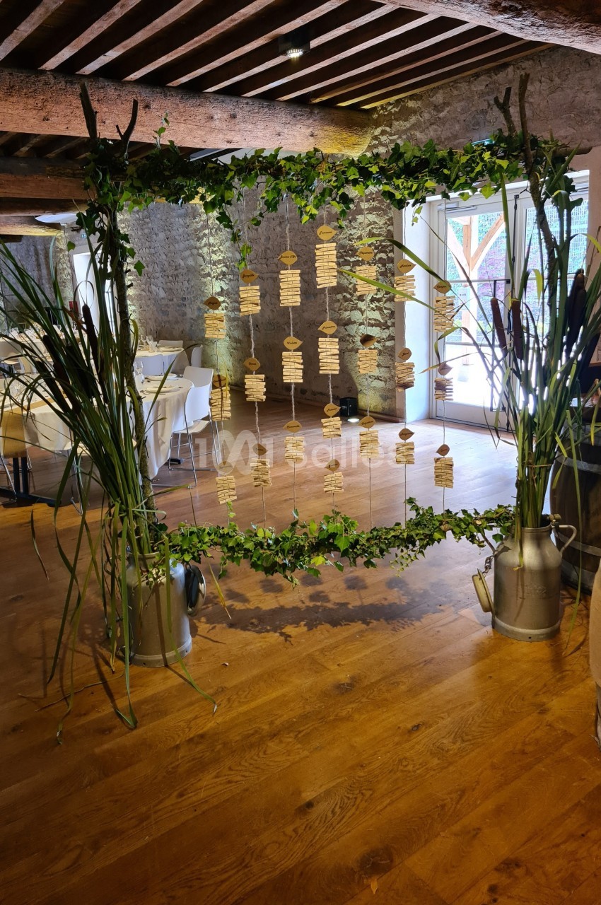 Cadre décoratif en bois et feuillage suspendant des étiquettes, installé dans une salle de réception rustique.