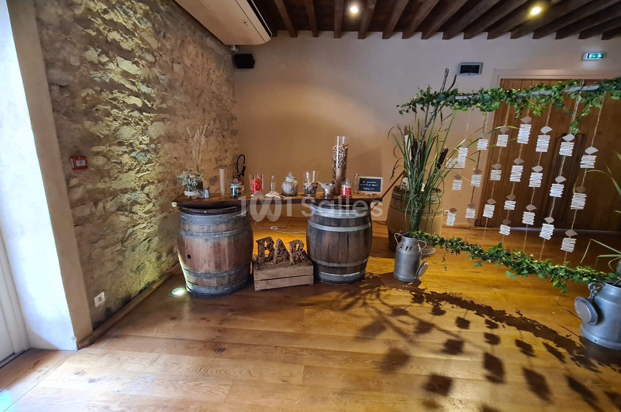 Deux tonneaux en bois formant un bar décoré, entourés de plantes et d'éléments rustiques dans une salle en pierre.