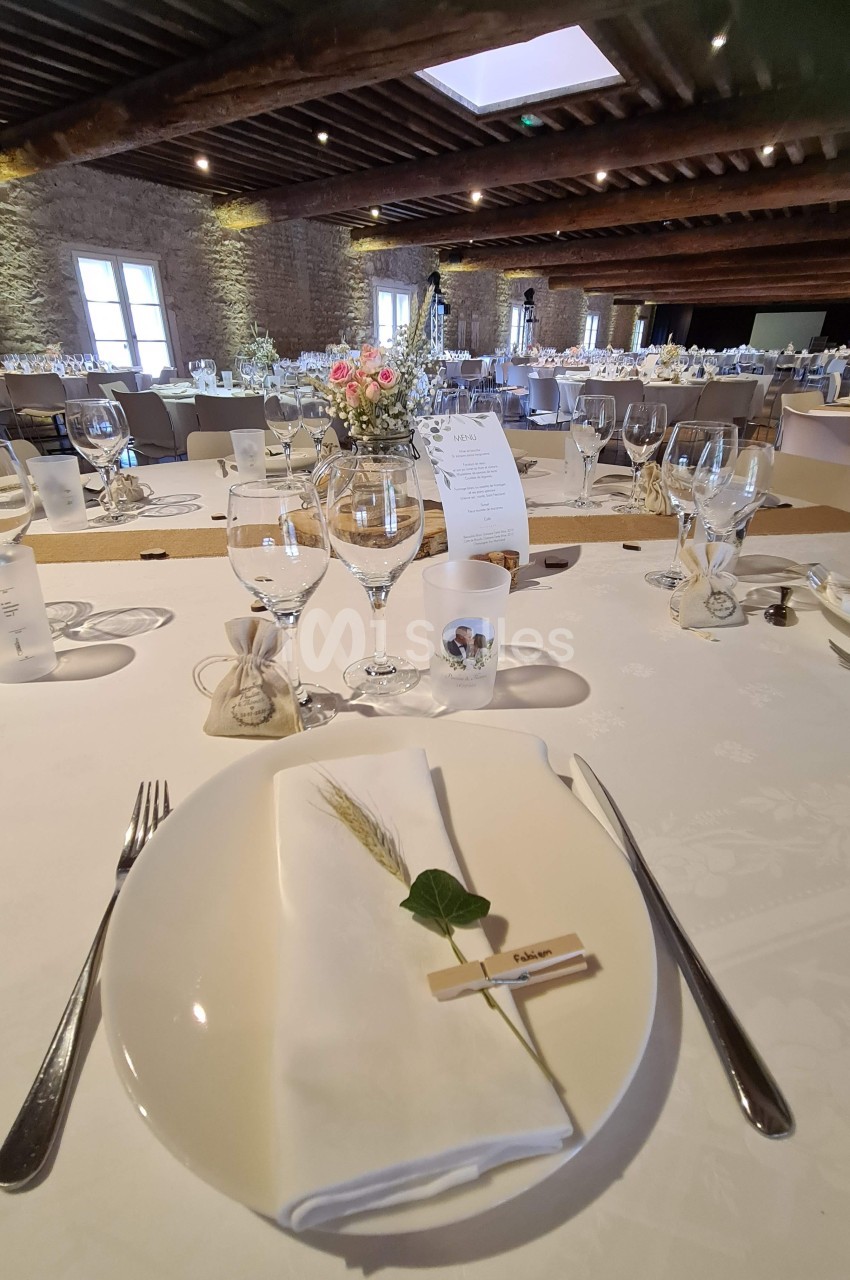 Table dressée pour un repas, avec assiette, serviette décorée, couverts, verres et centre de table floral dans une salle en…