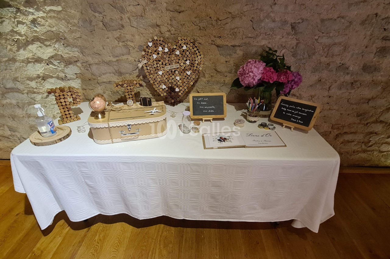 Table décorée pour un mariage avec urne, panneaux en ardoise, fleurs roses et mur en pierre en arrière-plan.