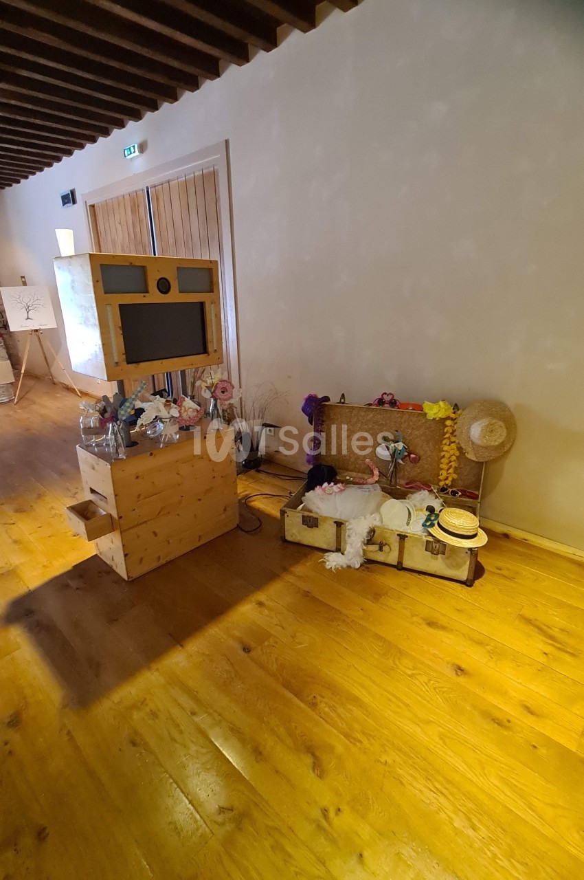 Photobooth en bois avec accessoires colorés disposés sur des valises anciennes dans une salle au sol en parquet.
