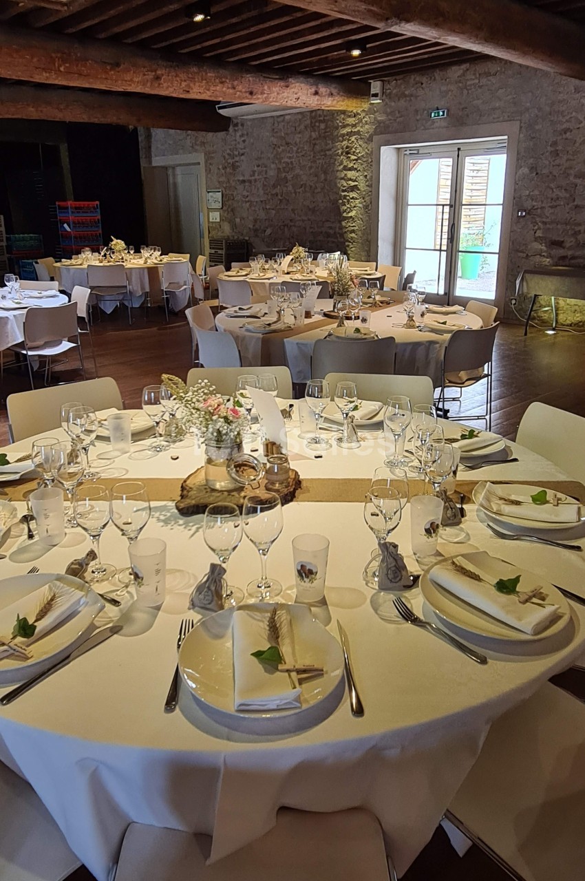 Salle de réception avec tables rondes dressées, nappes blanches, vaisselle élégante et décoration florale.