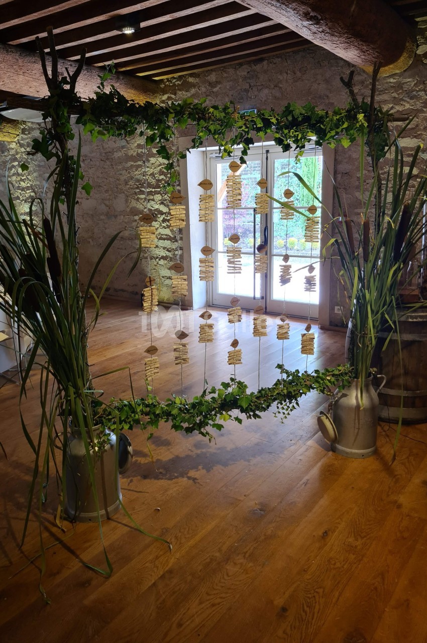 Structure décorative en lierre avec étiquettes suspendues, installée dans une salle en pierre avec parquet et poutres…