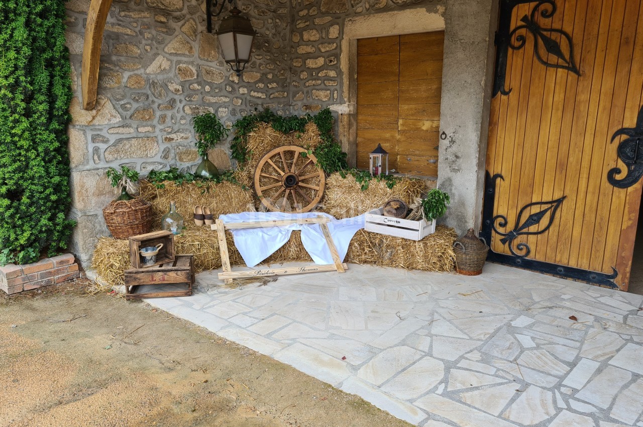 Décoration rustique avec bottes de paille, roue en bois, lanternes et objets anciens devant une porte en bois sculpté.