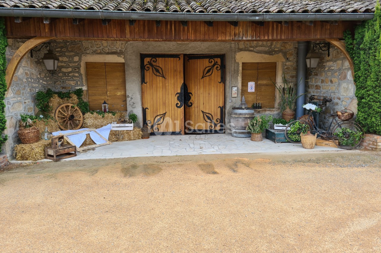 Entrée en bois sculpté d'un bâtiment en pierre, entourée de décorations rustiques avec plantes et objets anciens.