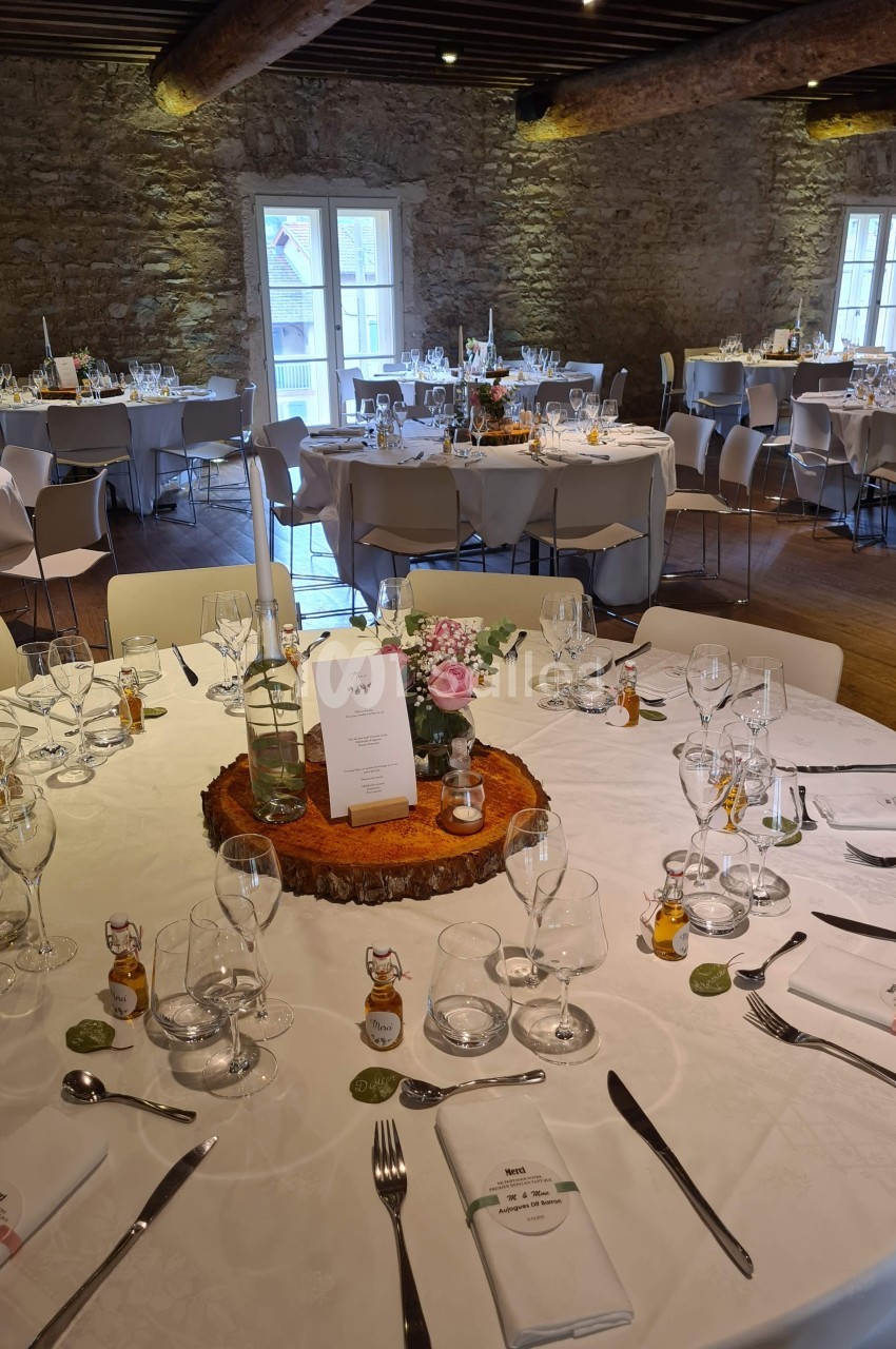 Salle de réception avec tables rondes décorées pour un événement, nappes blanches et centre de table floral.
