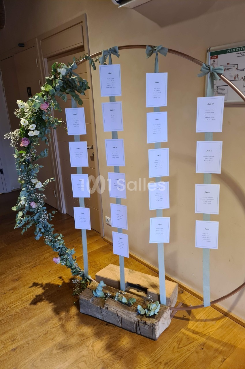 Cercle décoratif en métal avec fleurs et rubans, supportant des cartes de placement pour un événement.
