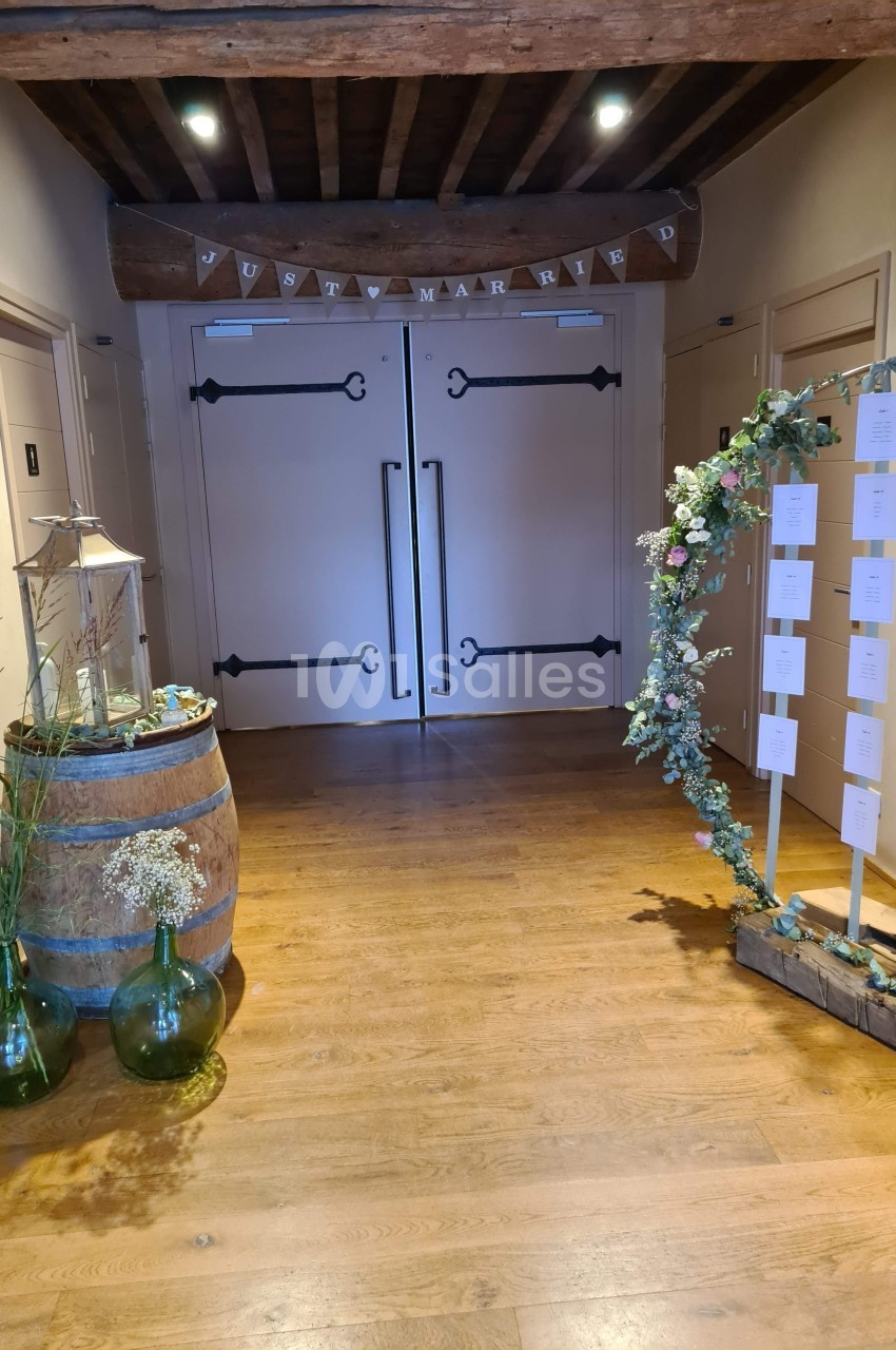 Entrée décorée avec des fleurs, un tonneau avec des vases et un panneau de plan de table, dans un intérieur en bois.