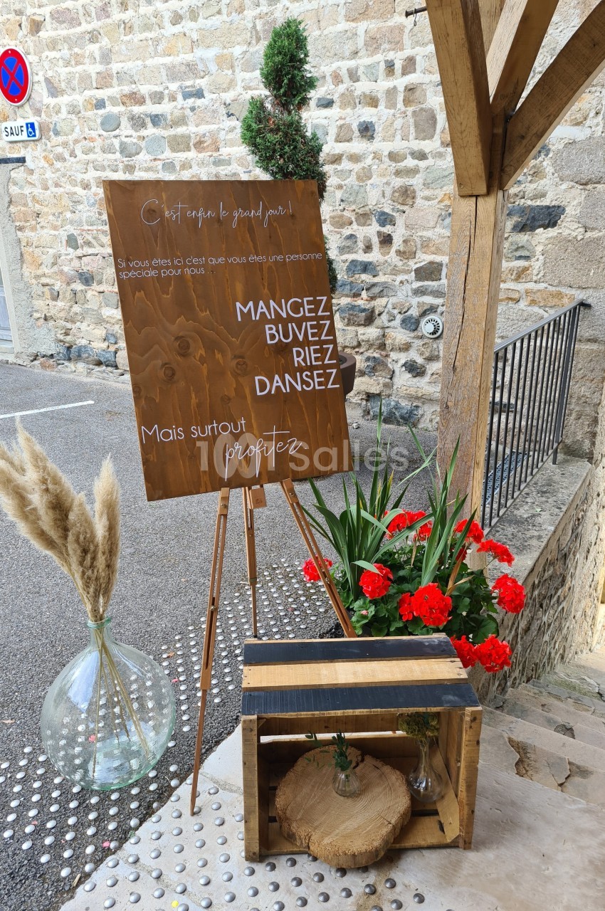 Panneau en bois avec un message festif, entouré de fleurs rouges, d'herbes séchées et d'une caisse décorative.