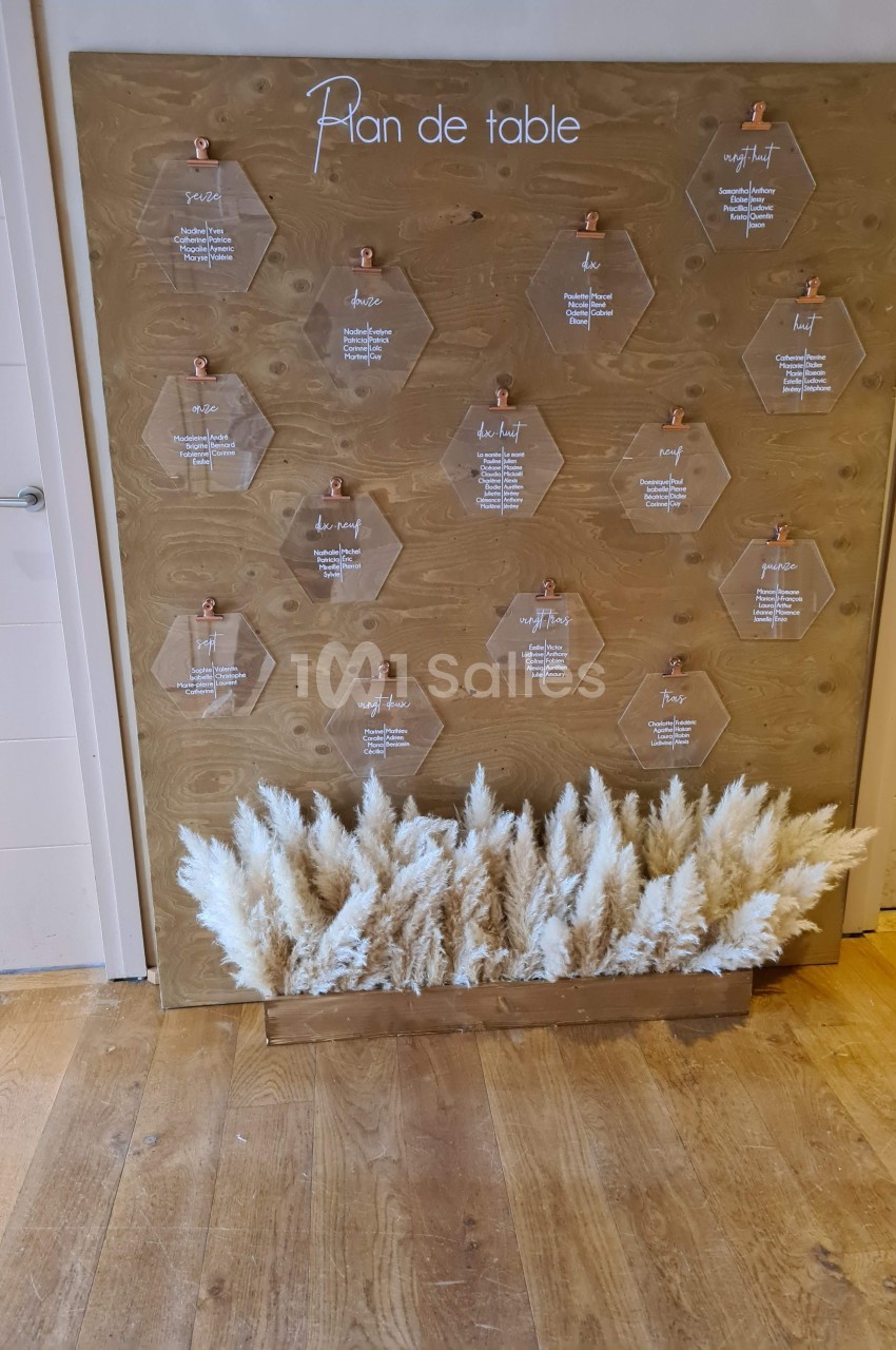 Plan de table sur un panneau en bois avec des hexagones transparents et un arrangement de pampas en bas.