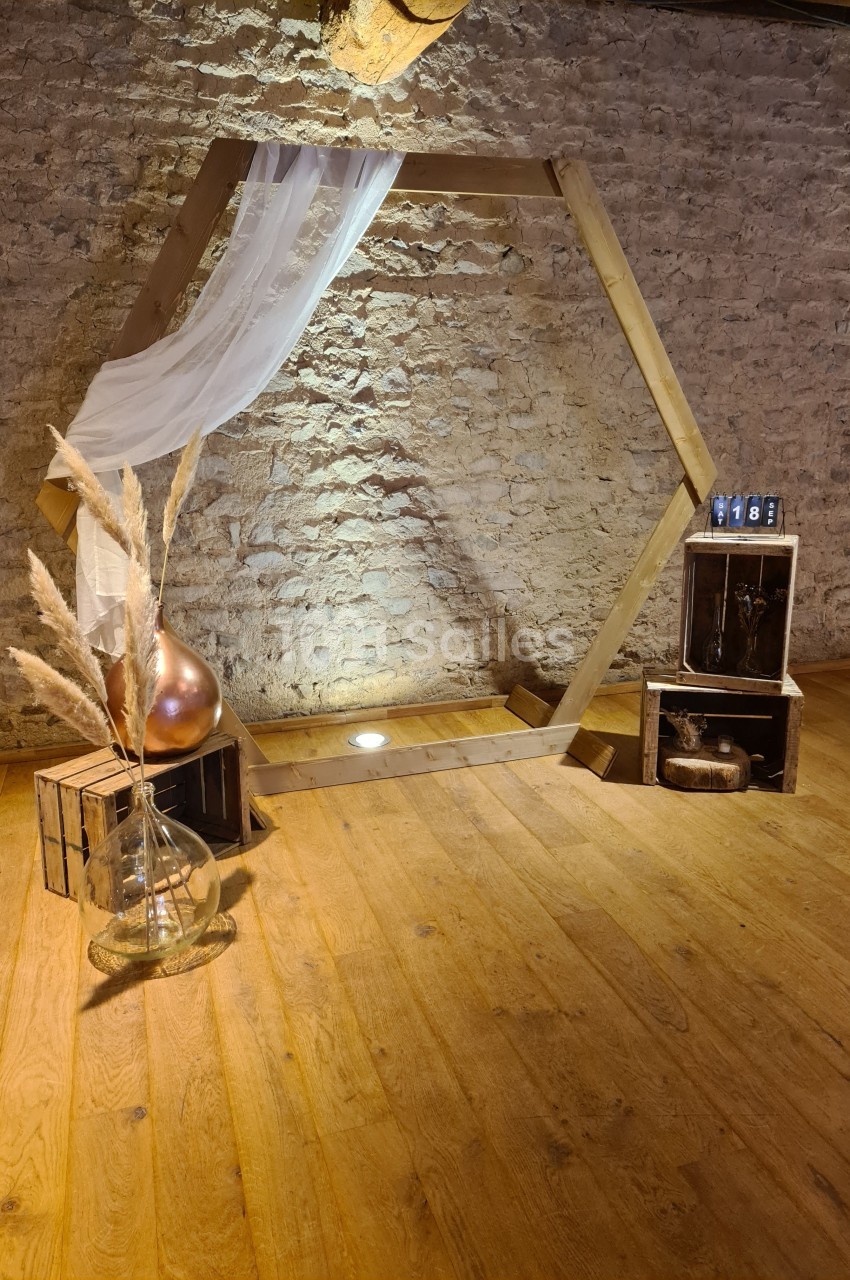 Structure hexagonale en bois décorée d'un voile blanc, entourée de caisses en bois, pampas et objets décoratifs.