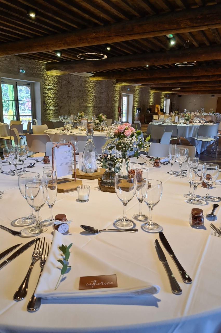 Salle de réception décorée pour un mariage, avec tables rondes dressées, fleurs et vaisselle élégante.