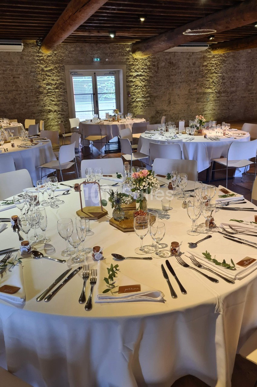 Salle de réception avec tables rondes décorées pour un événement, nappes blanches et arrangements floraux.