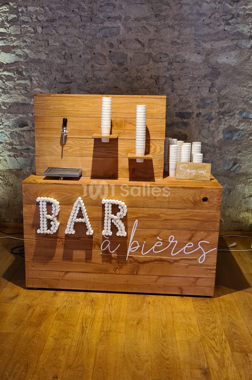 Comptoir en bois avec une inscription ’Bar à bières’, des gobelets empilés et un robinet de distribution.
