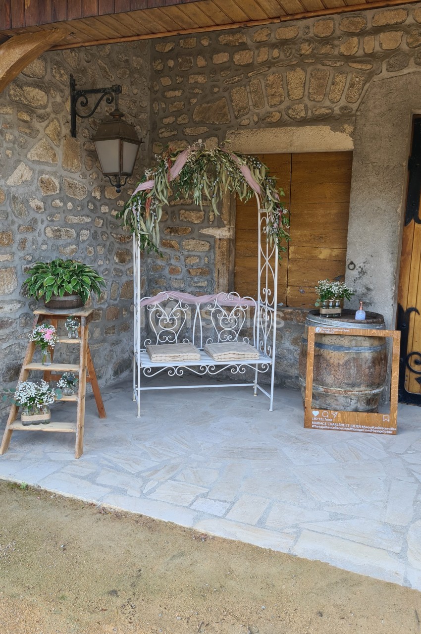 Banc en fer forgé décoré de feuillage, entouré de plantes et d'éléments rustiques sous un porche en pierre.