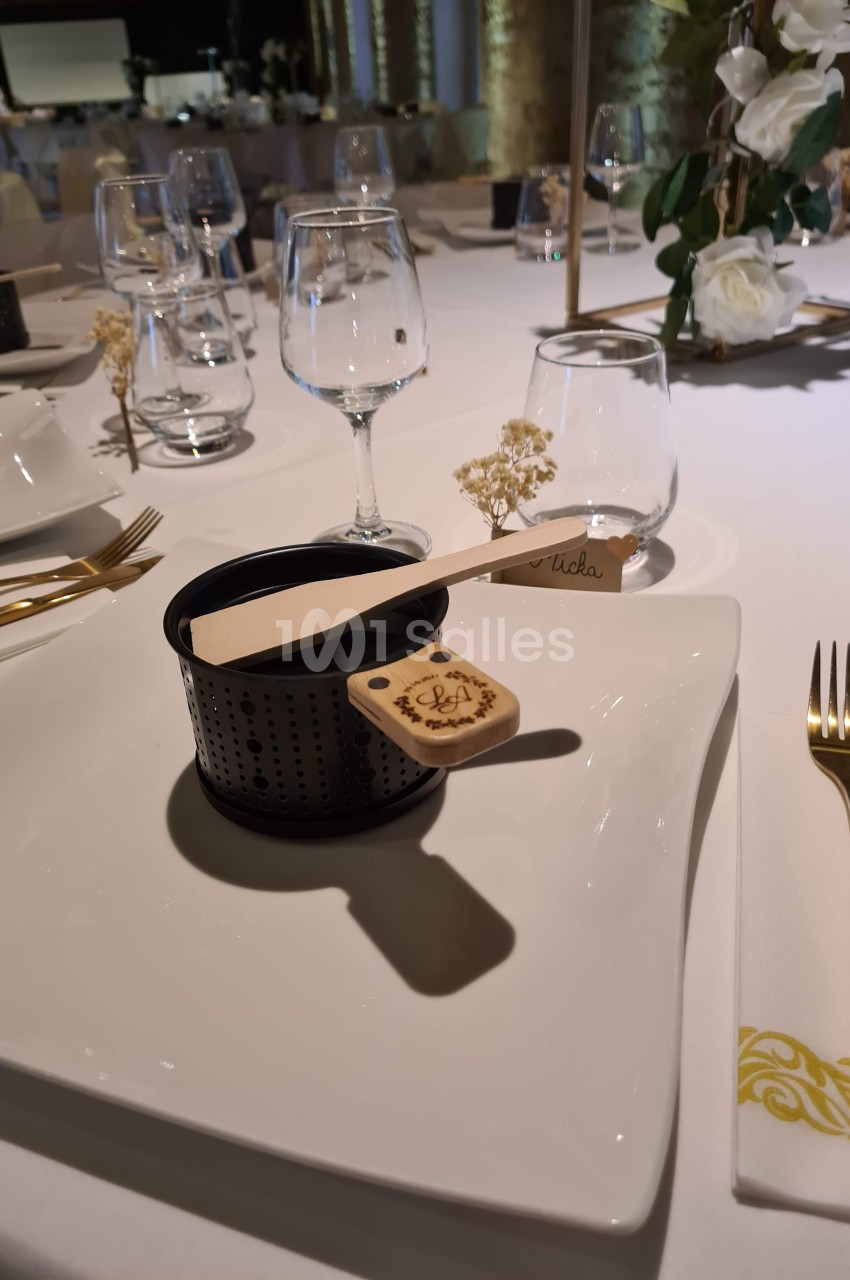 Service de table élégant avec assiette carrée, couverts dorés, verrerie et décoration florale raffinée.