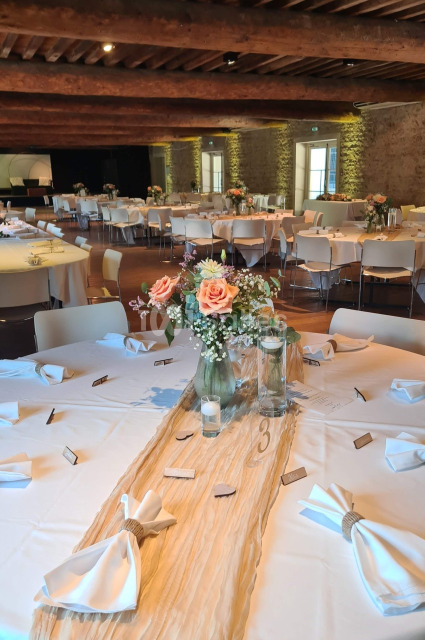 Salle de réception avec tables rondes décorées de nappes blanches, centres de table floraux et serviettes pliées.