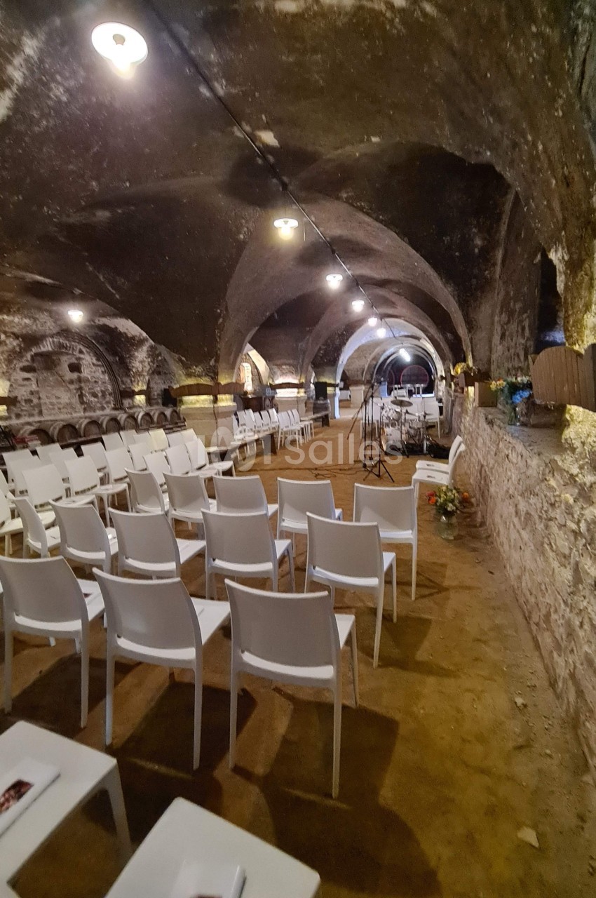 Chaises blanches alignées dans une cave voûtée en pierre, préparées pour un événement ou une cérémonie.