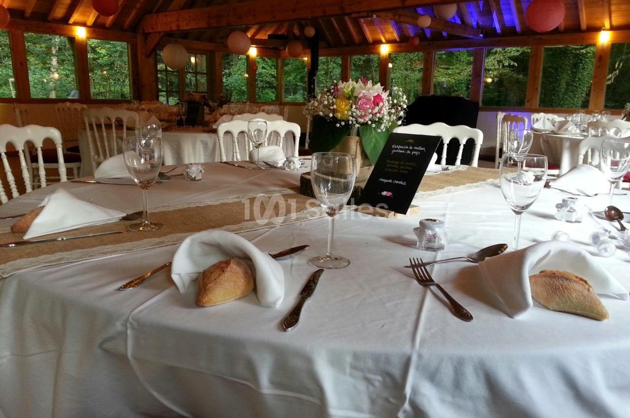 Table dressée pour un repas festif avec nappes blanches, verres, couverts, pain et centre de table floral.