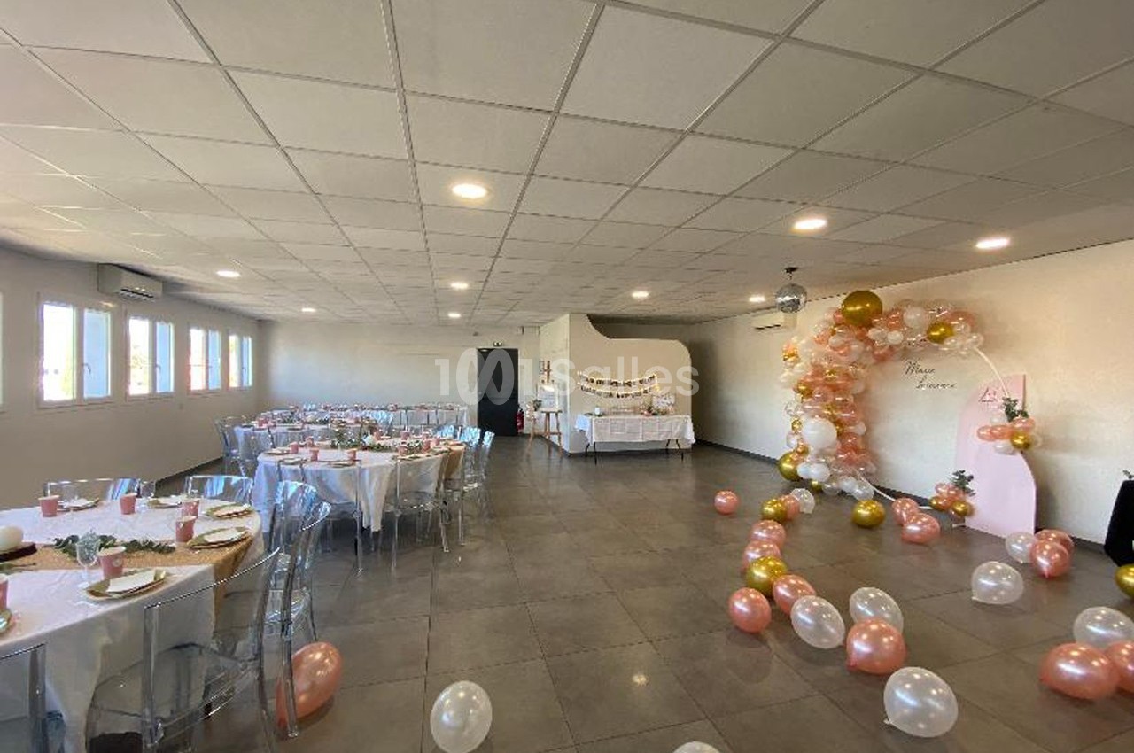 Salle décorée pour une fête avec tables dressées, ballons colorés et arche festive près d'une table de buffet.