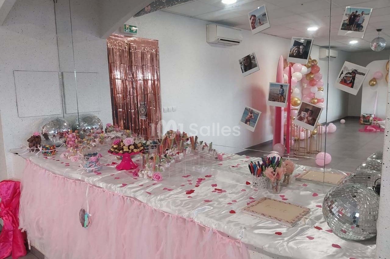 Table décorée pour une fête, ornée de nappes roses, confettis, bonbons, ballons et photos suspendues.