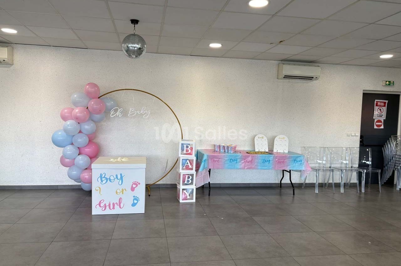 Salle décorée pour une fête de révélation de genre, avec ballons roses et bleus, table dressée et cubes ’BABY’.