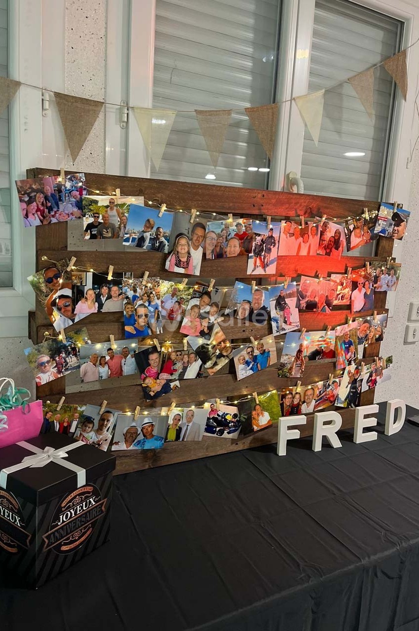 Mur décoratif avec des photos accrochées sur des planches en bois, guirlande lumineuse et lettres formant ’FRED’.