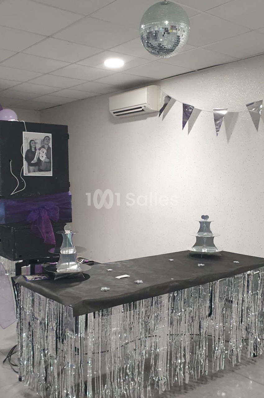 Table décorée avec des guirlandes argentées, une boule disco suspendue et un panneau avec une photo en noir et blanc.