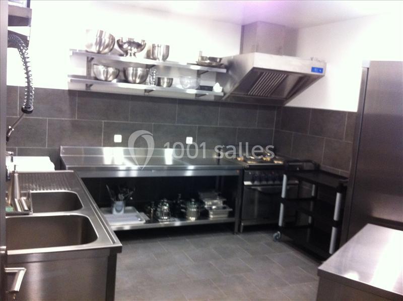 Cuisine professionnelle équipée avec plans de travail en inox, évier double, étagères murales et hotte d'extraction.
