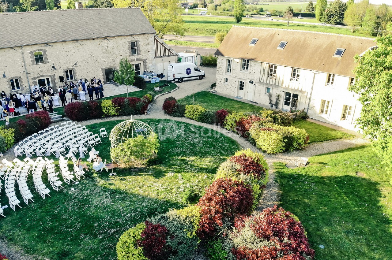 Vue aérienne d'un jardin aménagé pour un événement, entouré de bâtiments en pierre et de haies fleuries.