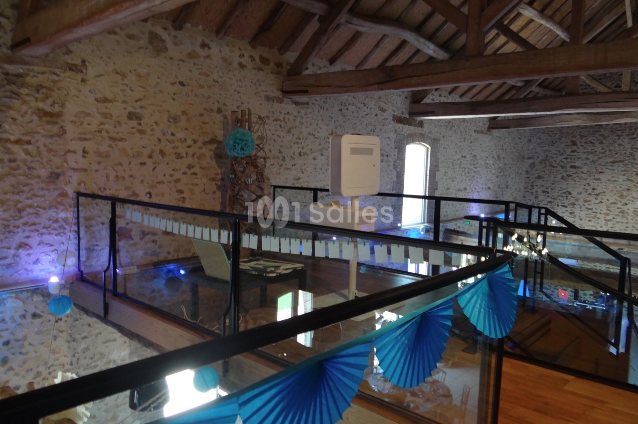 Mezzanine avec sol en verre, rambardes en métal et décoration bleue dans un intérieur en pierre apparente.