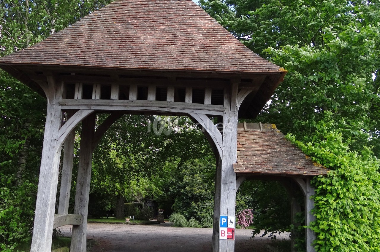 Portail en bois avec toit en tuiles, entouré de végétation, donnant accès à un chemin gravillonné.