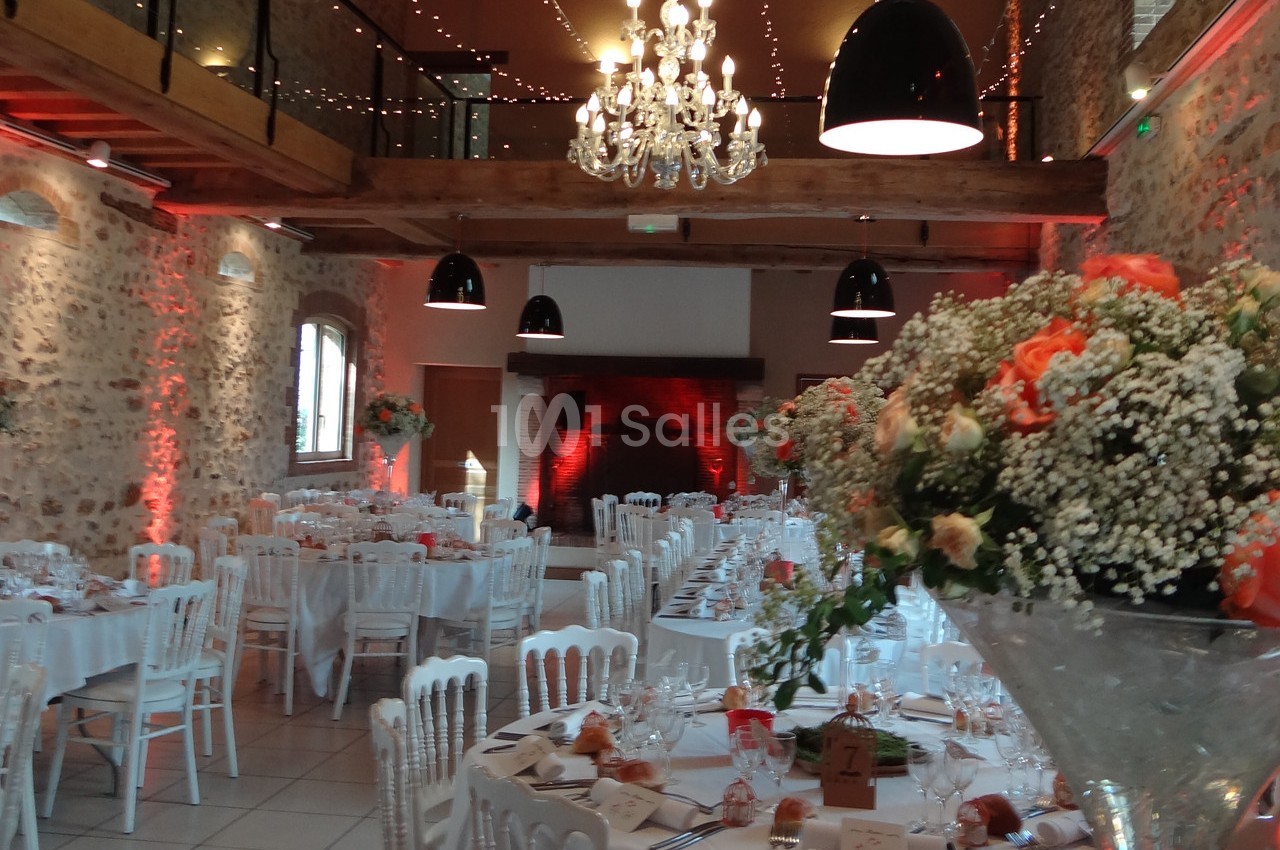 Salle de réception décorée avec des tables dressées, des fleurs et un éclairage chaleureux.